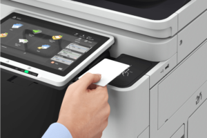 A hand holding a smart ID card over a badge reader on a copier.